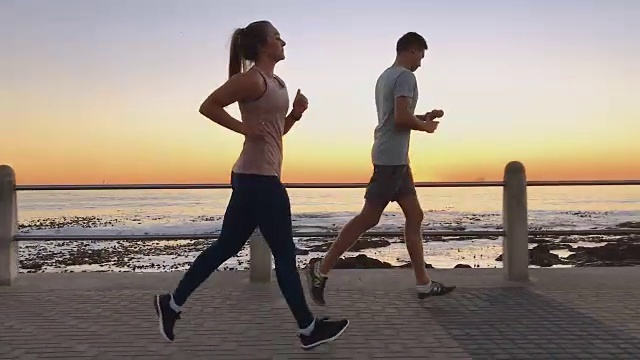 年轻和健康的运动员夫妇慢跑在日落海边散步