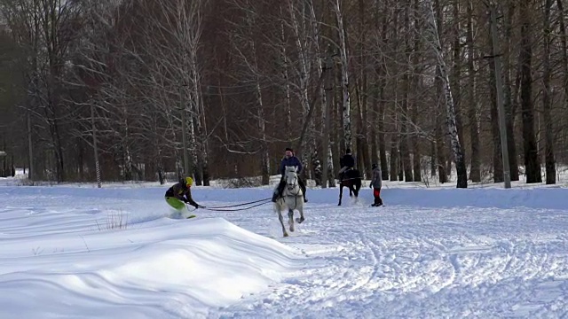 慢镜头:一个女孩骑着马疾驰。一匹马用绳子拖着一个滑雪者。滑雪者在雪堆中骑在滑雪板上。女子骑师和男子滑雪板训练成对。