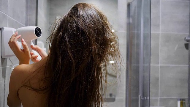 护发年轻女子在浴室对着镜子用电吹风吹湿头发