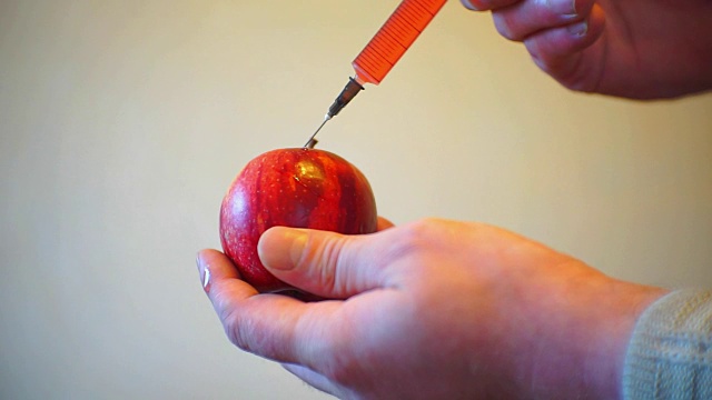 男性用注射器在一个成熟的苹果上注射