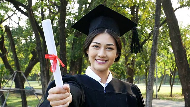 年轻的亚洲女学生戴着毕业帽和礼服，花园背景，女性与毕业概念。