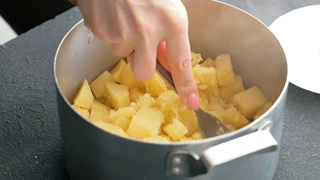 特写女子用叉子在炖锅里做土豆泥的手。烹饪土豆泥。