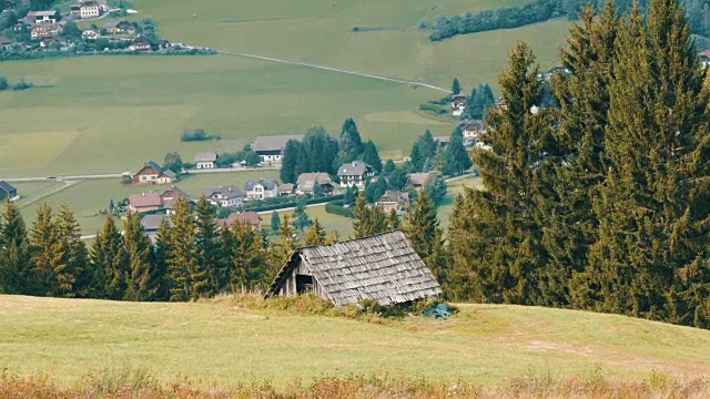 舒适的非常古老的木屋在奥地利阿尔卑斯山的一个小山上，绿色的草在新的现代房子的背景，古老的乡村木屋在村庄