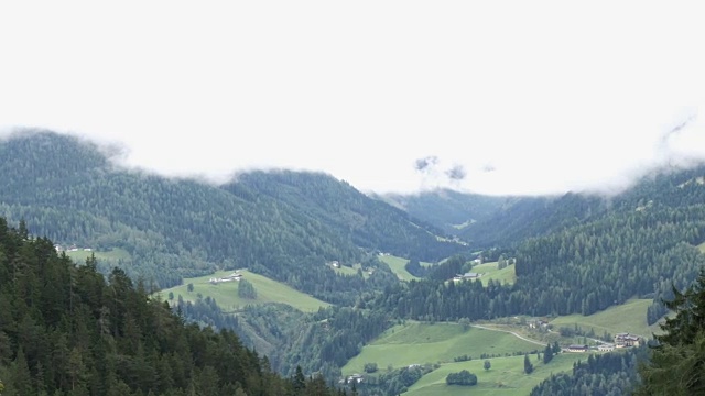 奥地利阿尔卑斯山山谷的风景。山谷中有许多房屋，四周群山环绕。白色的房屋和教堂，绿色的草地牧场。美丽的村庄