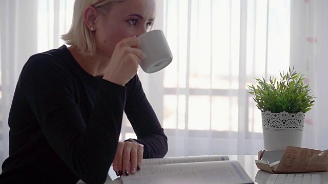 侧视图。年轻的女商人坐在桌子旁，在笔记本上记笔记。桌上放着电脑、智能手机和一杯咖啡。学生在网上学习。博主。