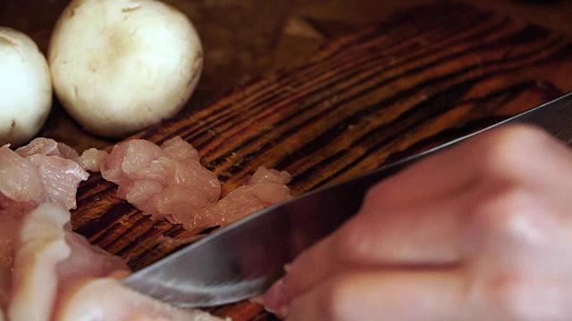 女人在家里的厨房里把鸡胸肉切成小块