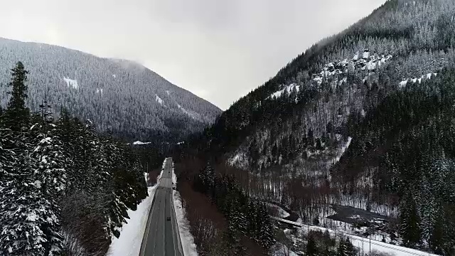 一辆黑色汽车沿着河边的乡村森林公路行驶，雪天空中拍摄