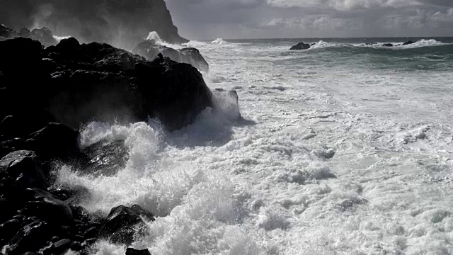 浪花从汹涌的波浪漂流到高岩石露头。慢动作镜头