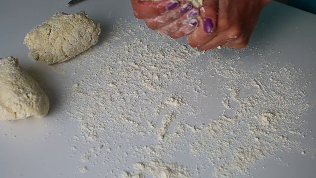 女人为懒惰的vareniki铺开面团，在桌子上撒上面粉。