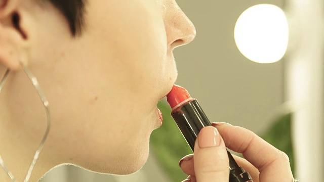 近距离看女人化妆和涂口红。美丽的女人用红色口红在性感的嘴唇和看化妆镜