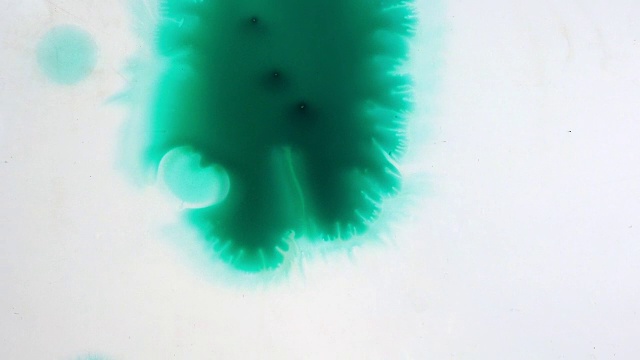 墨水在玻璃上流动，并向不同的方向扩散。墨水滴下来，在白色的背景上扩散。近距离观察流动的墨水。视频和运动图形的模板