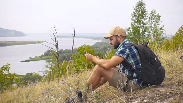 游客他坐在山上，用平板电脑。背着背包的男人在树林里。徒步旅行。森林之旅。露营。休闲。生态旅游。野外。冒险开始了。