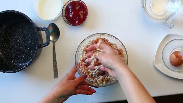 一个女人正在做肉丸子。将肉末与磨碎的奶酪、米饭和鸡蛋混合。