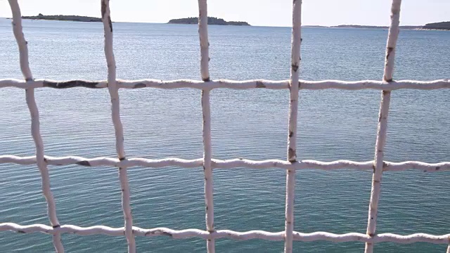 铁栅栏和蓝色的大海在背景。安全网远眺大海，特写。旧的生锈的白色高钢栅栏，有天空和海滩。地中海,亚得里亚海。阳光明媚的夏天的一天。