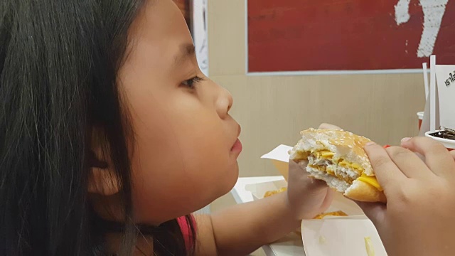 饥饿的女孩吃快餐，孩子在餐厅吃汉堡，