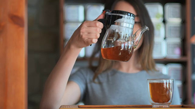 详情图-年轻微笑的女人从玻璃壶倒红茶到小杯子