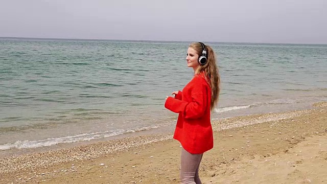 这个女人在海边的海滩上戴着大耳机听音乐