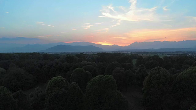 空中:俯瞰乡村、森林林地和自然公园，意大利皮埃蒙特阿尔卑斯山脉的日落五彩天空