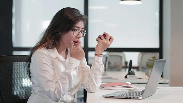 一个美丽而健康的女商人，一边啃着苹果一边处理笔记本电脑的业务任务。