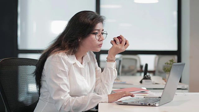 详情图-一个美丽而健康的女商人，一边啃着苹果一边处理笔记本电脑的业务任务。
