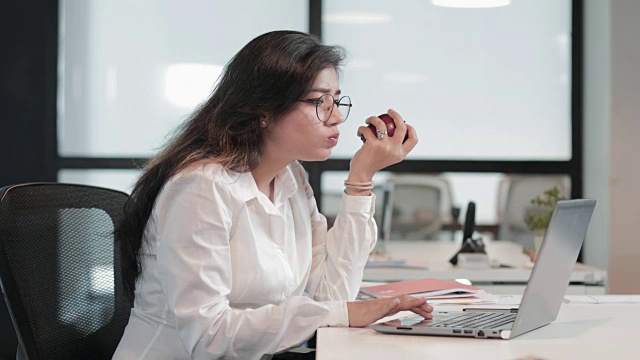 详情图-一个美丽而健康的女商人，一边啃着苹果一边处理笔记本电脑的业务任务。