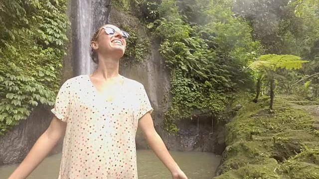 年轻女子在巴厘岛的瀑布上凝视大自然，享受大自然的新鲜。人们出行绿色环保理念。慢动作拍摄