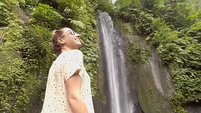 年轻女子在巴厘岛的瀑布上凝视大自然，享受大自然的新鲜。人们出行绿色环保理念。慢动作拍摄