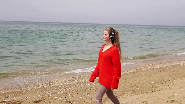 这个女人在海边的海滩上戴着大耳机听音乐