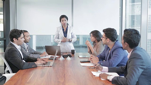 一个自信的，积极的和独立的女商人给一群办公室职员在会议室。