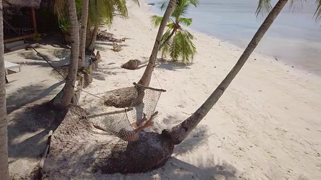 热带气候下，年轻男子在海滩边的吊床上休息。人们旅游度假放松的概念。4K分辨率的视频，在菲律宾拍摄
