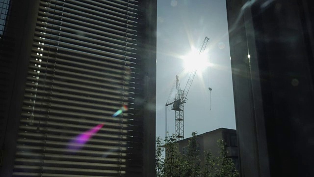 太阳在房屋和建筑塔吊的映衬下移动。窗外的景色