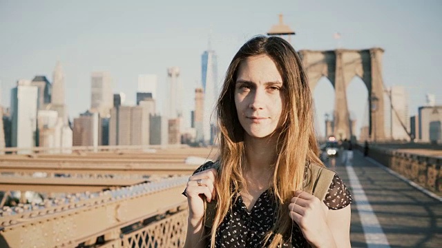 年轻积极的女性白人游客背包看相机，微笑在阳光灿烂的布鲁克林大桥，纽约4K