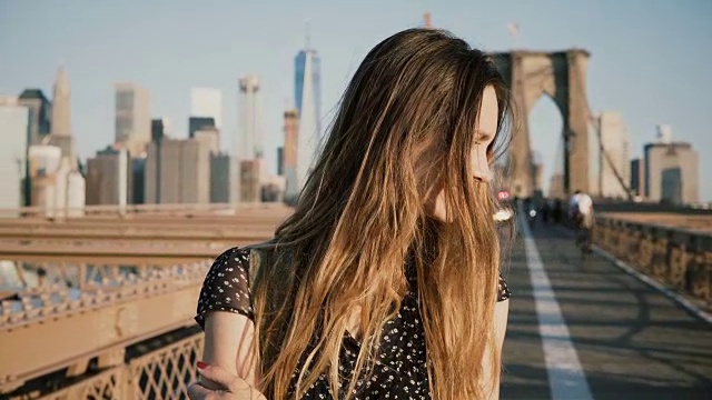 美丽的白人女孩享受温暖阳光明媚的天气，回头看镜头微笑在布鲁克林大桥4K