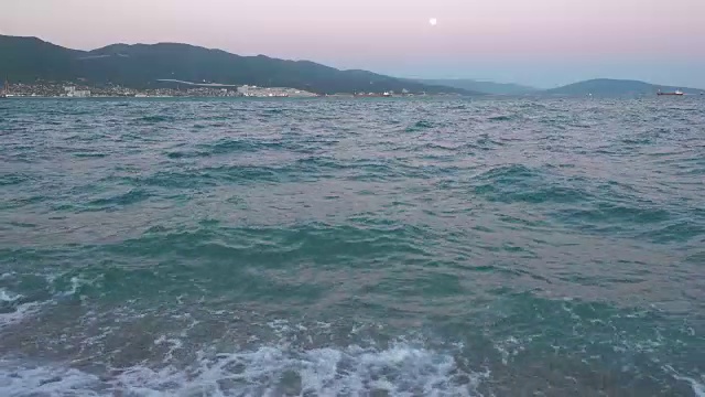美丽的日落在暴风雨的海上。远处的港口城市。