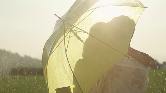 近距离观察:恋爱中的男人和女人躲在雨伞后面，在乡下接吻