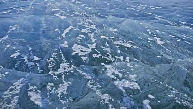 雪在冰面上飞舞。雪花在贝加尔湖的冰面上飞舞。冰非常美丽，有独特的裂缝。雪花闪耀着红光。在日落时分。高对比度。