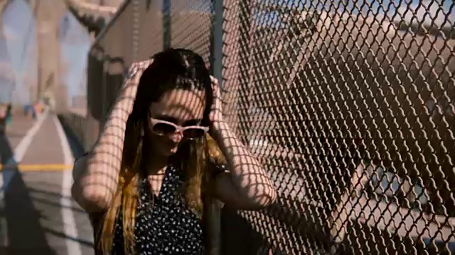 详情图-美丽的欧洲女人戴着时尚的太阳镜走向相机，触摸头发在布鲁克林大桥的影子护栏4K