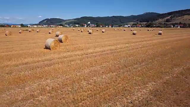 在有圆草堆的田野上空低空飞行。风景如画的小村庄和山峦为背景。