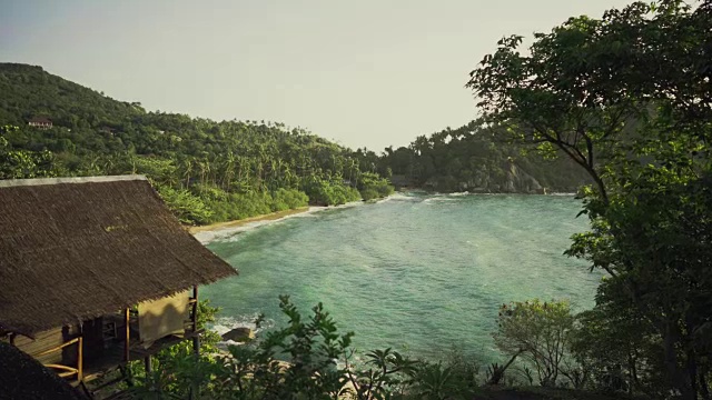 航拍的美丽的海湾与大海浪和甜美的丛林山丘在岸边。小屋可见。