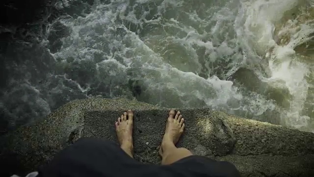 高角度拍摄的人的腿站在靠近海边的岩石上的垃圾和垃圾漂浮在海岸附近。
