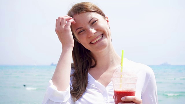 素食女人与草莓冰沙对抗大海的慢动作。健康女性享受健康的生活方式