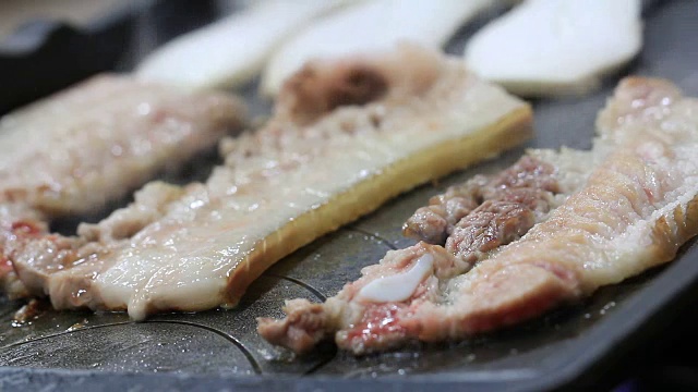 五花肉或三层猪肉烧烤称为samgyeopsalgui，油性食物烹调在韩国烧烤盘，与生菜叶，紫苏叶，泡菜白萝卜，青葱沙拉