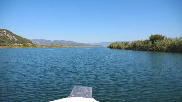 在阳光明媚的日子里，从船首看到沿着海湾移动的美丽景色。漂浮在河上的帆船，以蓝天和山景为背景。暑假或假期的概念。近距离观点