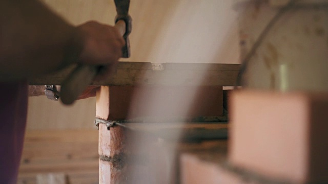 建筑工正在用锤子敲打一块红砖，然后把它弄平。一个建筑工人正在建一个砖砌壁炉