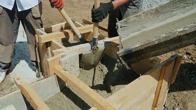 在建筑工地使用混凝土。工人们把混凝土放进一个木模里。建筑工地繁重的体力劳动