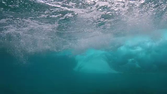 水下:强大的深蓝色桶状海浪将无法辨认的冲浪者推向岸边