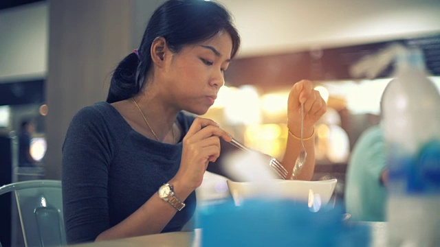 年轻的亚洲女士吃面汤在美食广场色调的视频