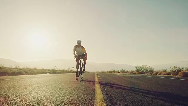 慢镜头近距离的男子骑在公路上的自行车在沙漠道路上在阳光明媚的一天与镜头光晕