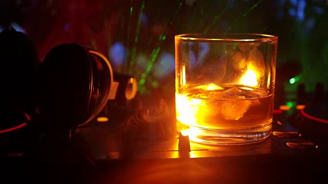 詳情圖-在夜總會(huì)的dj控制器上，裝有冰塊的威士忌酒杯。在迪斯科燈光下的夜總會(huì)音樂派對上，一杯威士忌上戴著Dj耳機(jī)。滑塊拍攝