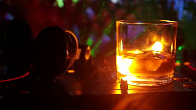 詳情圖-在夜總會(huì)的dj控制器上，裝有冰塊的威士忌酒杯。在迪斯科燈光下的夜總會(huì)音樂派對上，一杯威士忌上戴著Dj耳機(jī)。滑塊拍攝